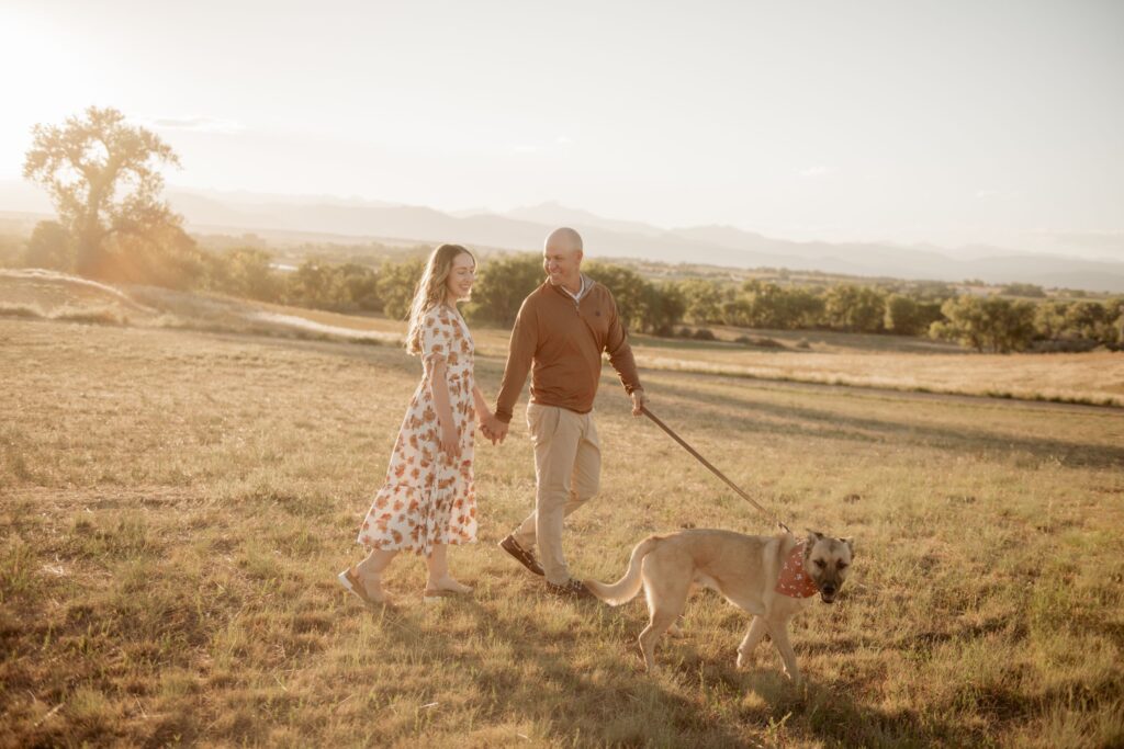Couple Walking Dog Through Golden Field During Sunset