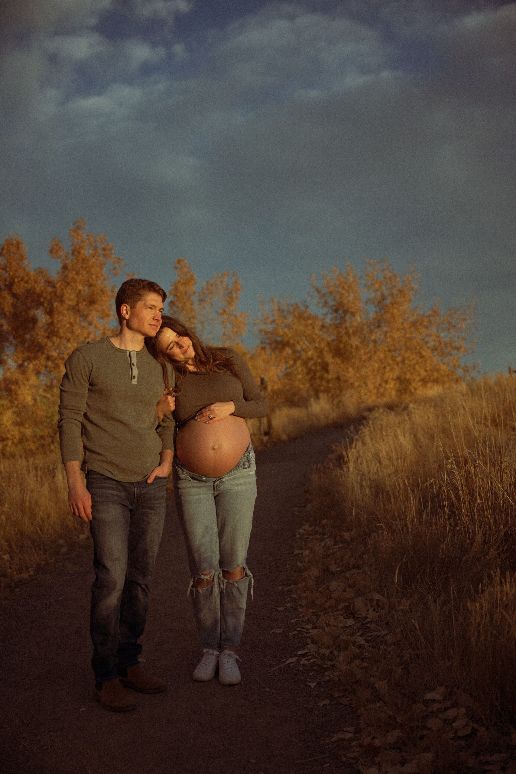Couple standing on a path, cradling her baby bump.