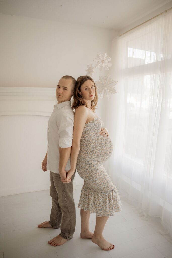 Expecting couple posing together in a bright indoor maternity photoshoot