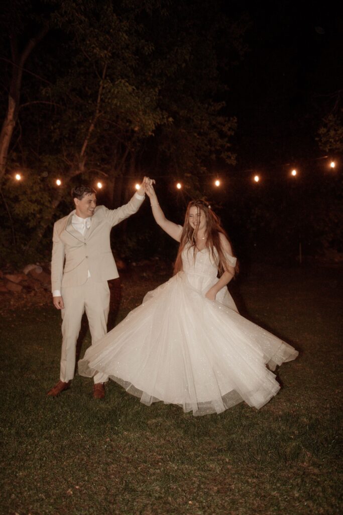 Groom twirling bride under string lights.