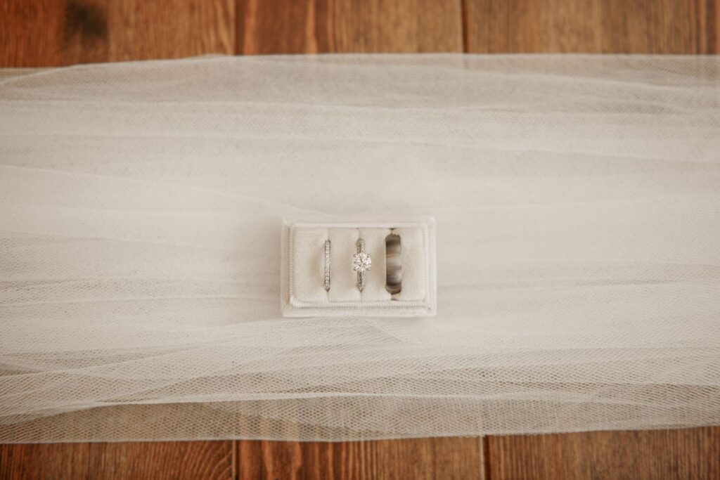 Wedding rings displayed in a velvet ring box on a bridal veil.