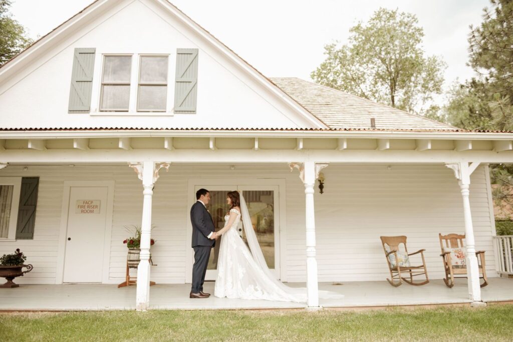 Bride and groom standing together on the porch of a white farmhouse.