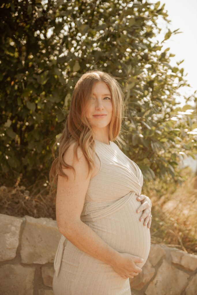 Pregnant woman in beige dress posing outdoors for maternity photoshoot