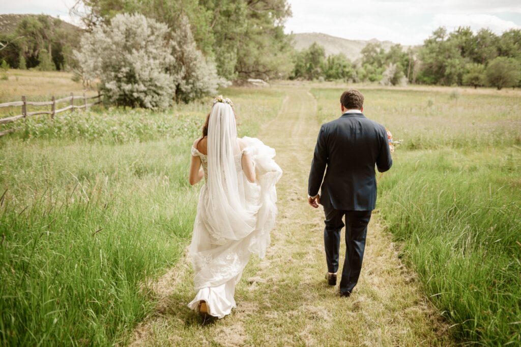 Bride and groom walking hand in hand down a grassy path in a mountain meadow
