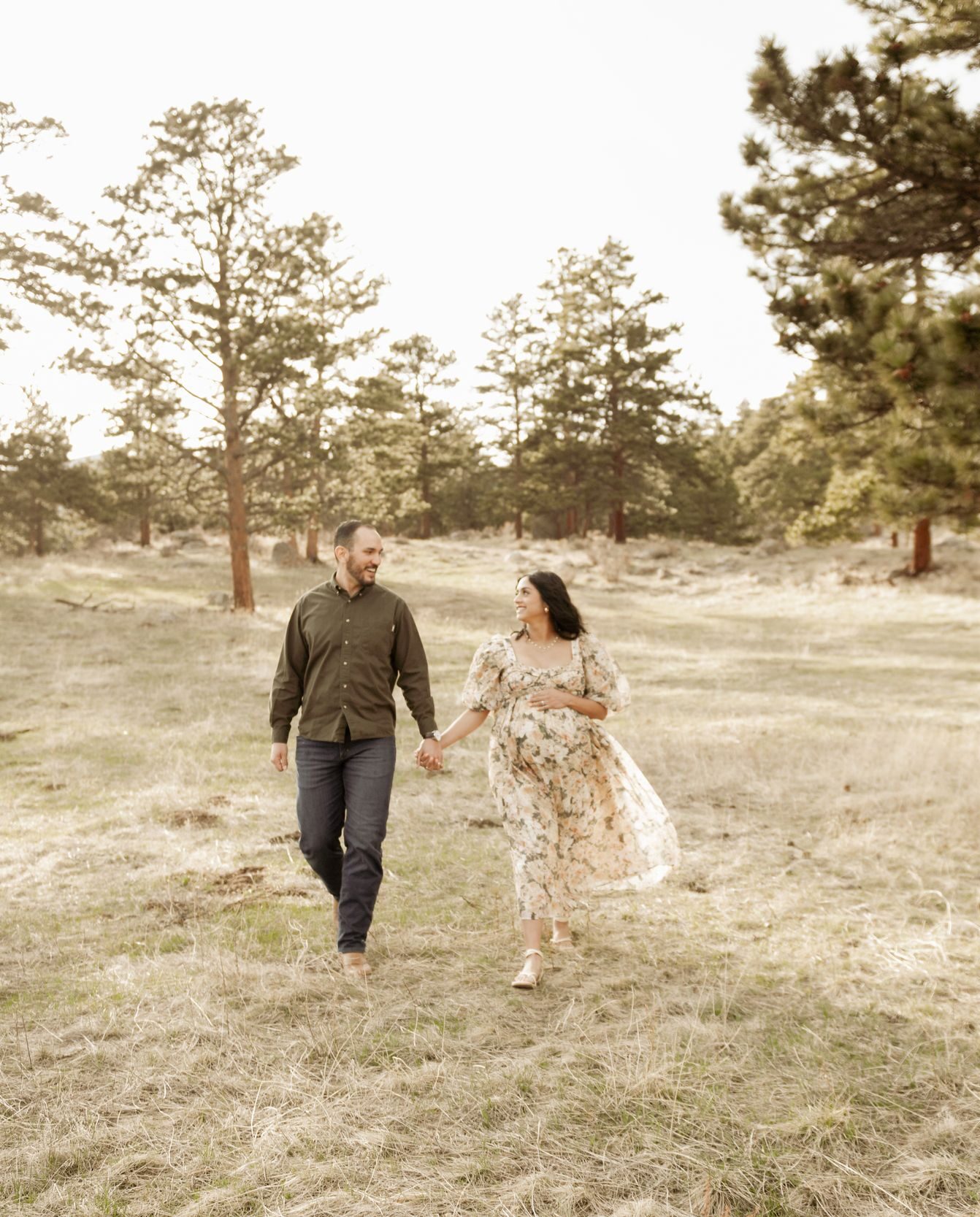 Expectant couple walking hand in hand through a scenic field during a maternity photoshoot.