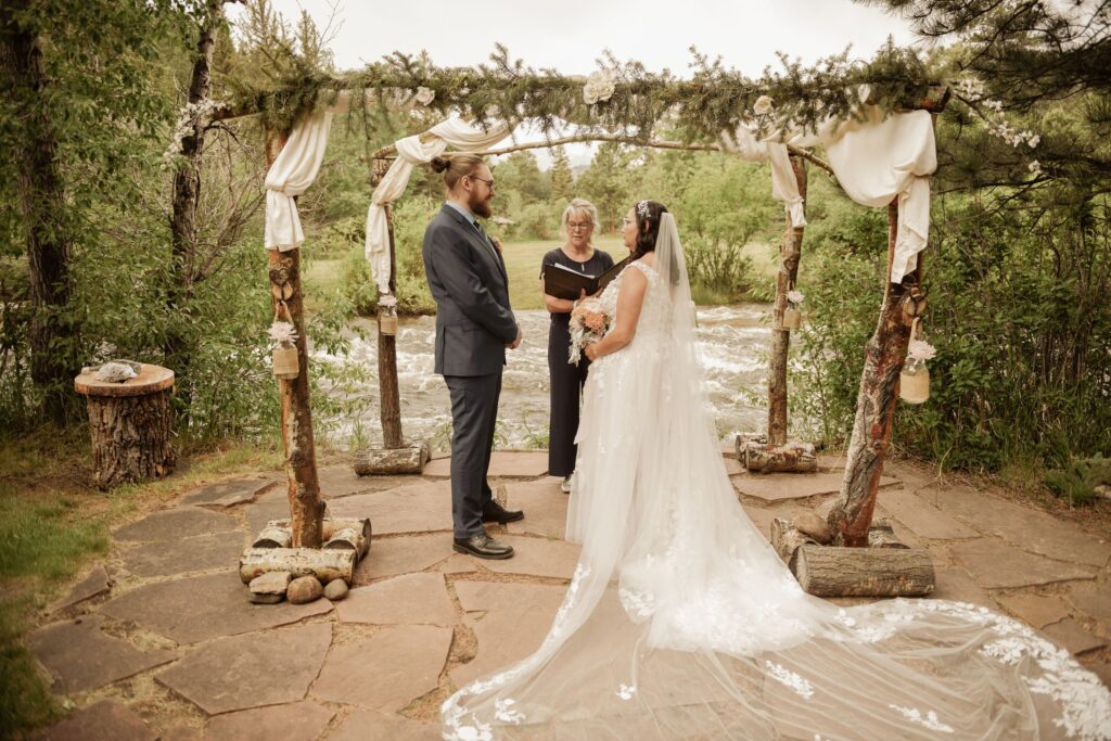 Bride and groom exchanging vows under a rustic wedding arch