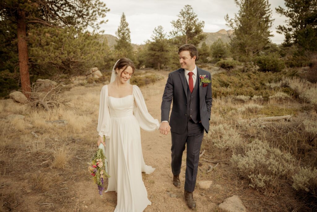 Bride and groom walking hand in hand on a scenic mountain trail after their wedding.