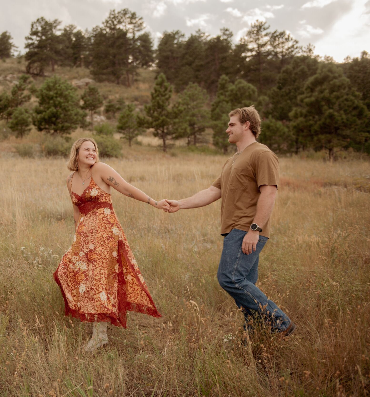 Couple holding hands and smiling in a grassy field during an engagement session.