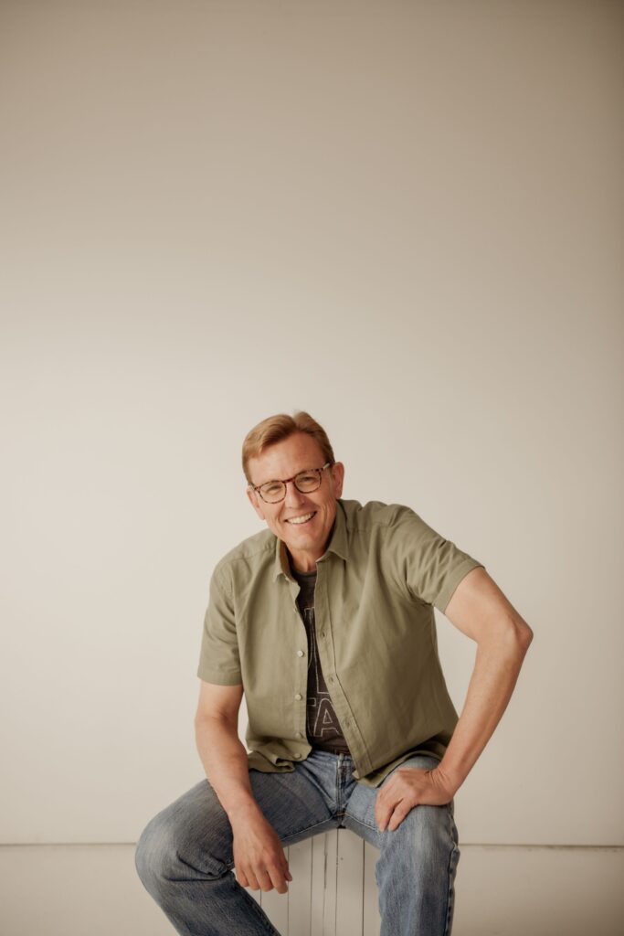 Man smiling while seated for a professional portrait in a studio.