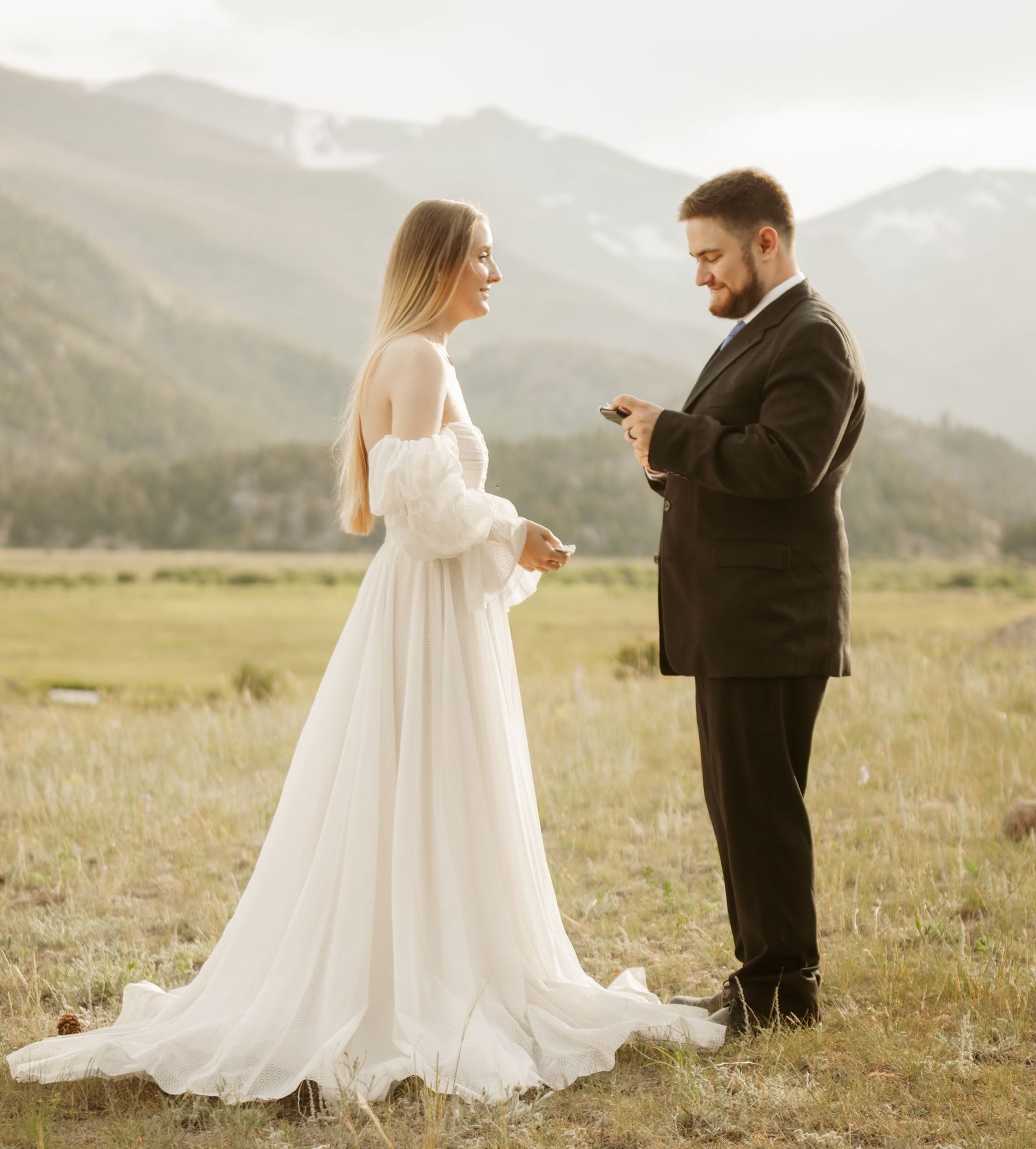 Bride and groom exchanging vows in a mountain meadow during an outdoor wedding ceremony.