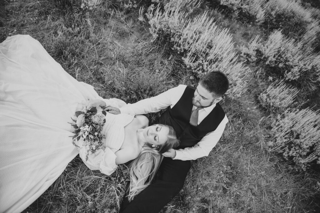 Black and white overhead photo of a bride and groom lying together in a grassy field.