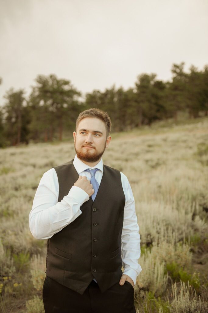 Groom adjusting his tie during an outdoor mountain wedding portrait.