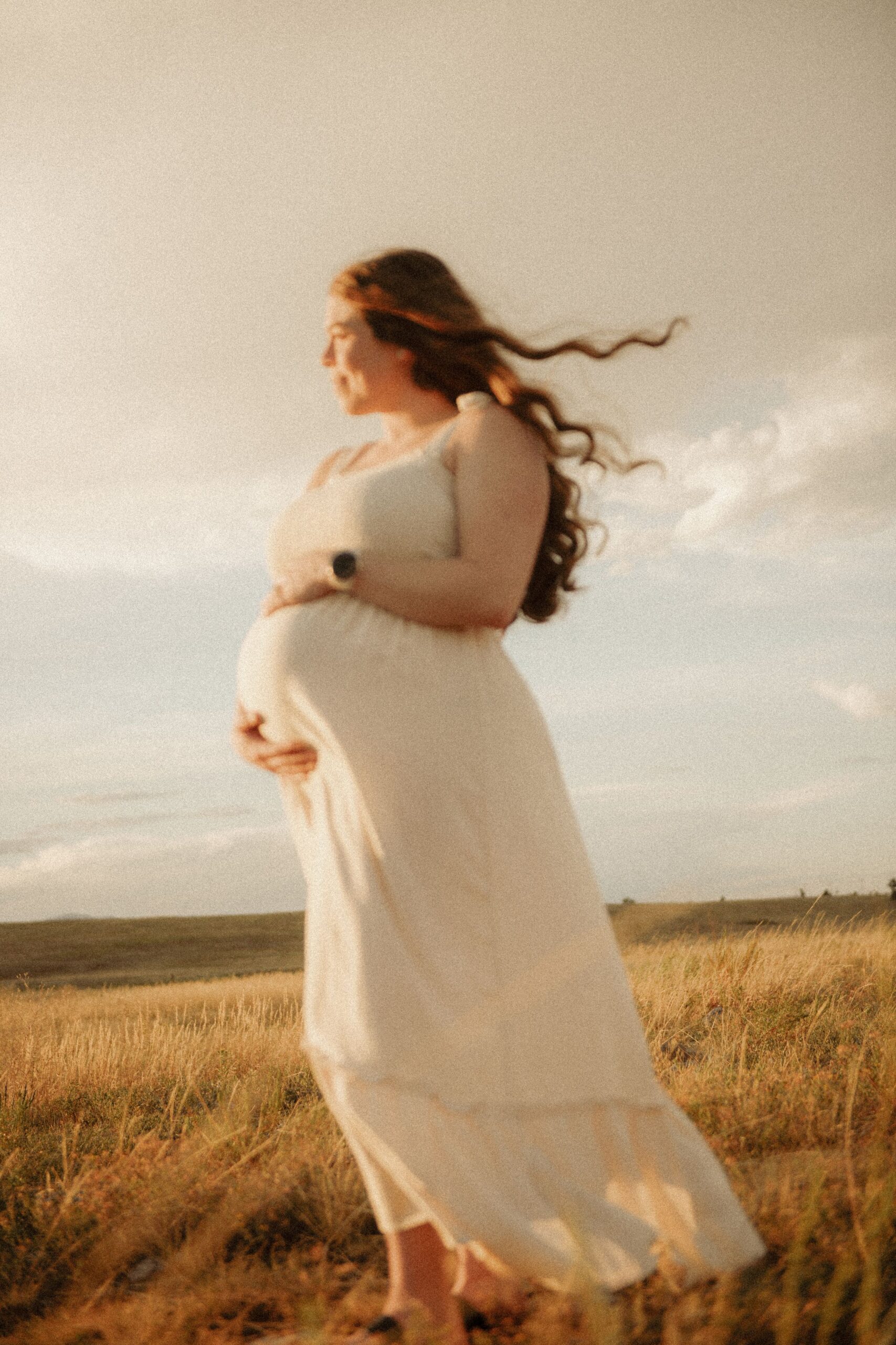 Pregnant woman in flowing white dress standing in a golden field