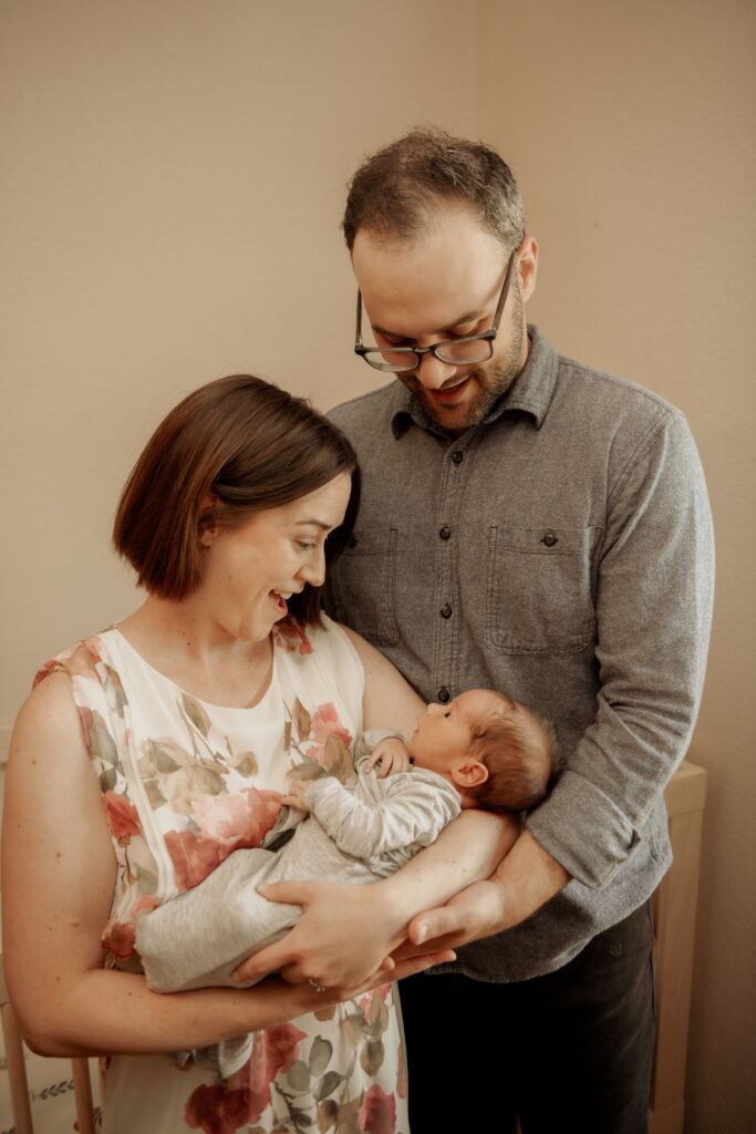Parents smiling while holding their newborn baby indoors.