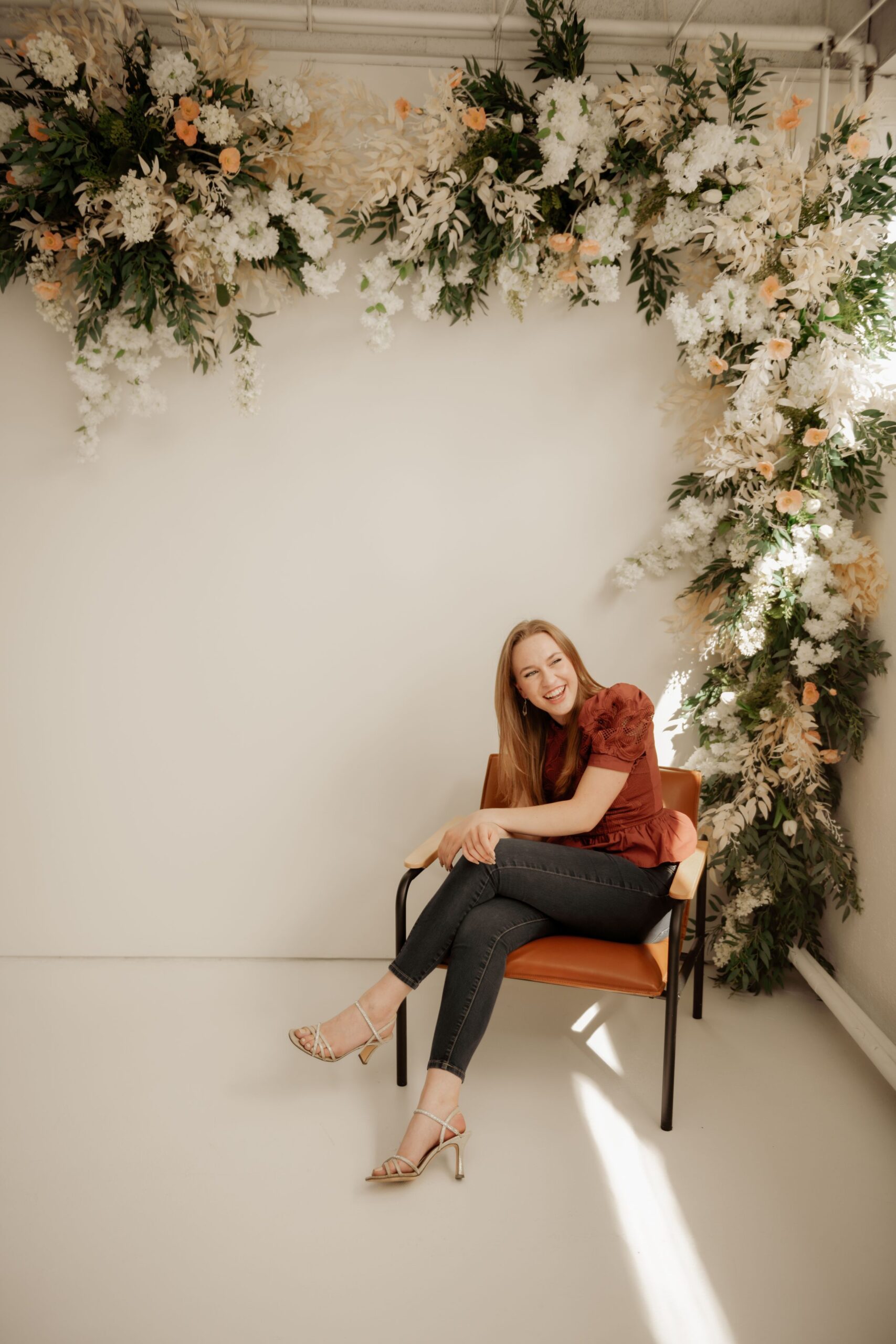 Woman seated beneath a floral installation in a bright studio.