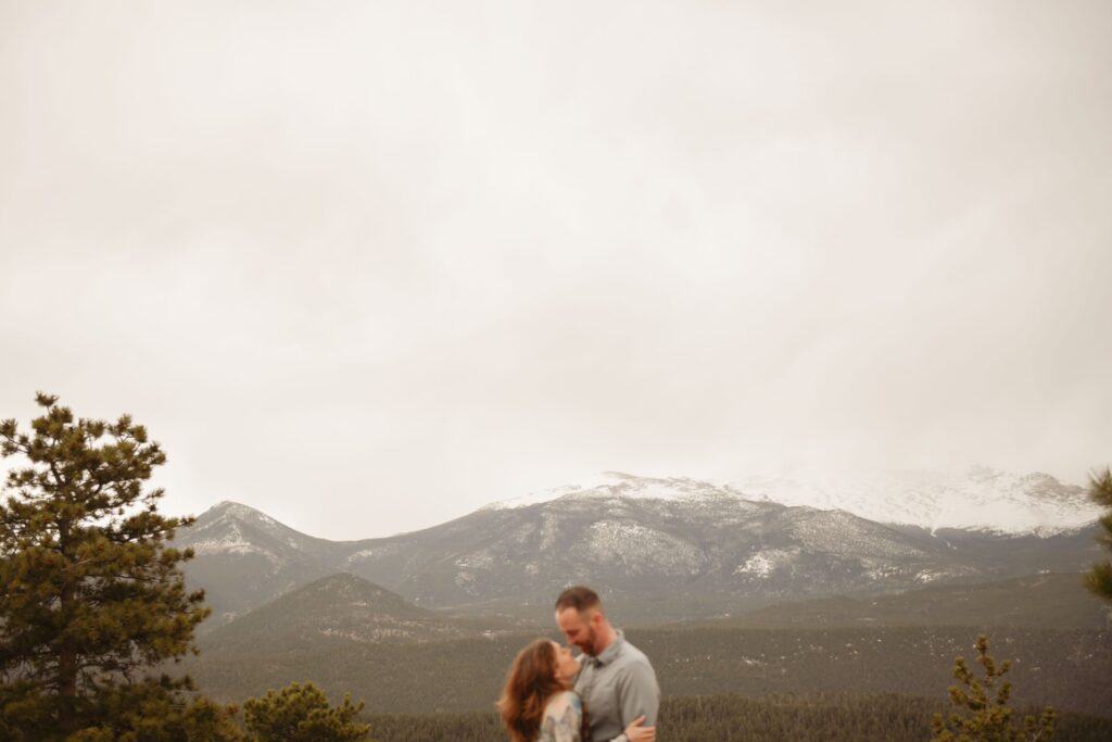 Couple kissing with snow-capped mountains in the background.
