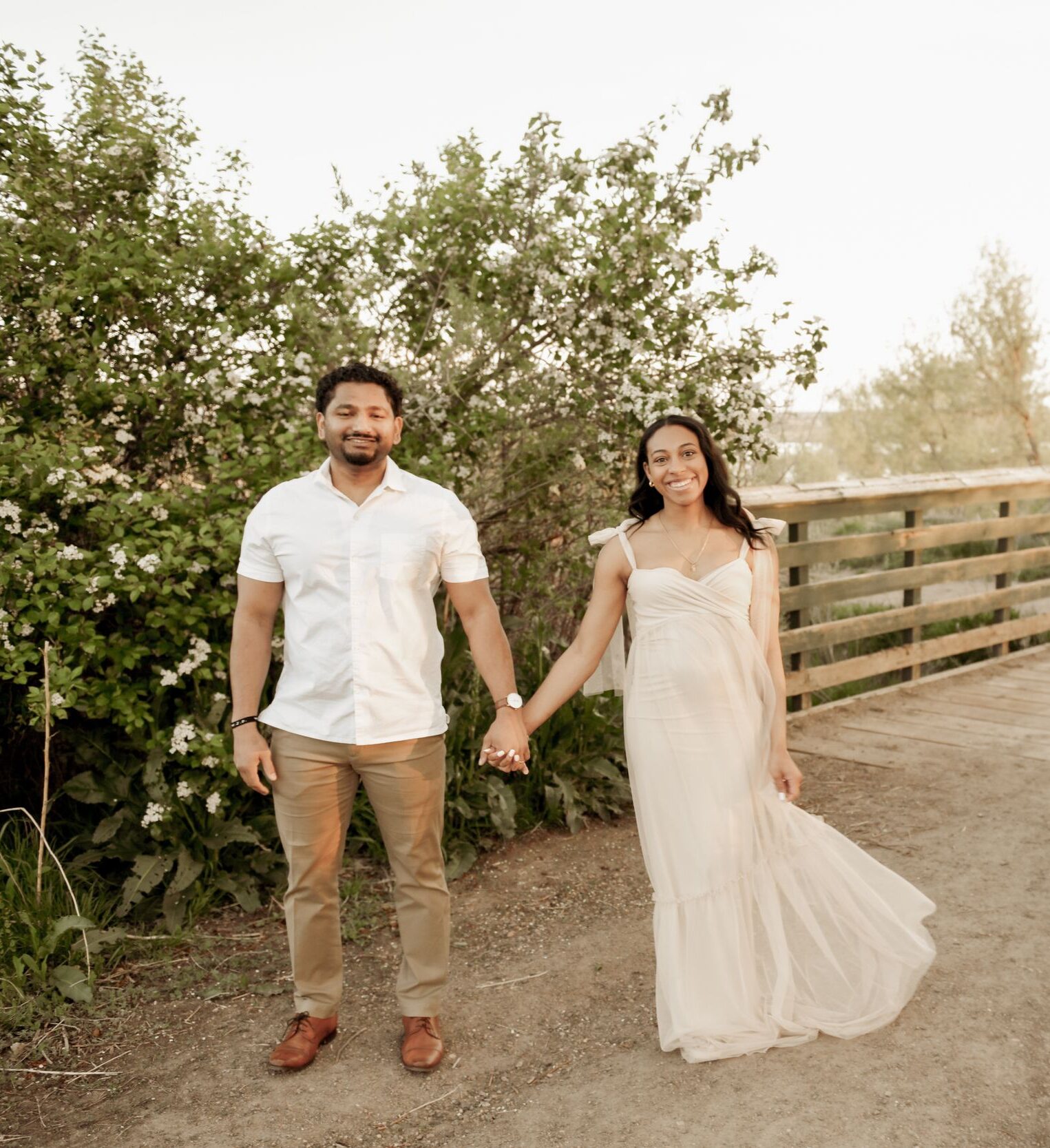 Couple holding hands walking on a boardwalk trail.