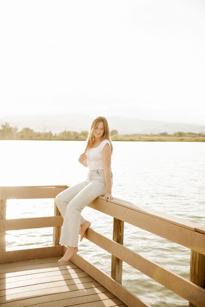 Woman sitting on a dock railing by a lake.