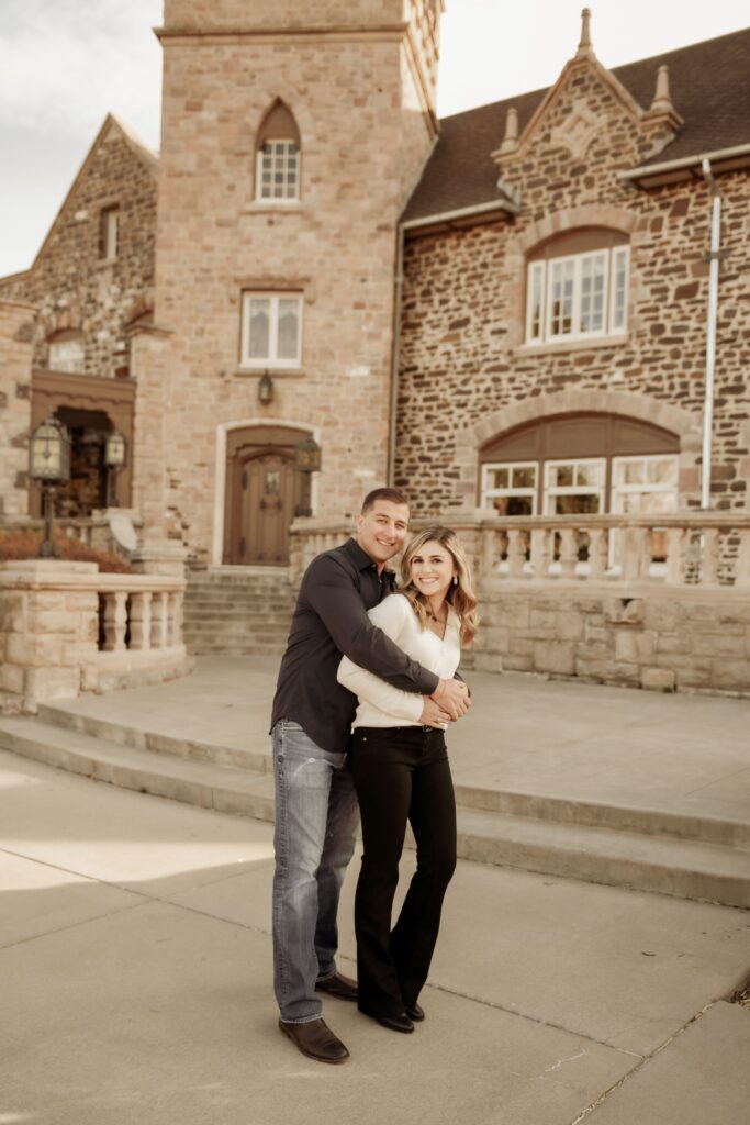 Engaged couple hugging in front of a stone castle building. Highlands Ranch Mansion