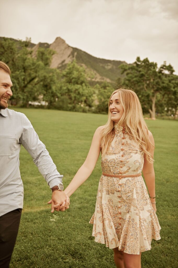 Couple laughing and holding hands in a park with mountains behind.