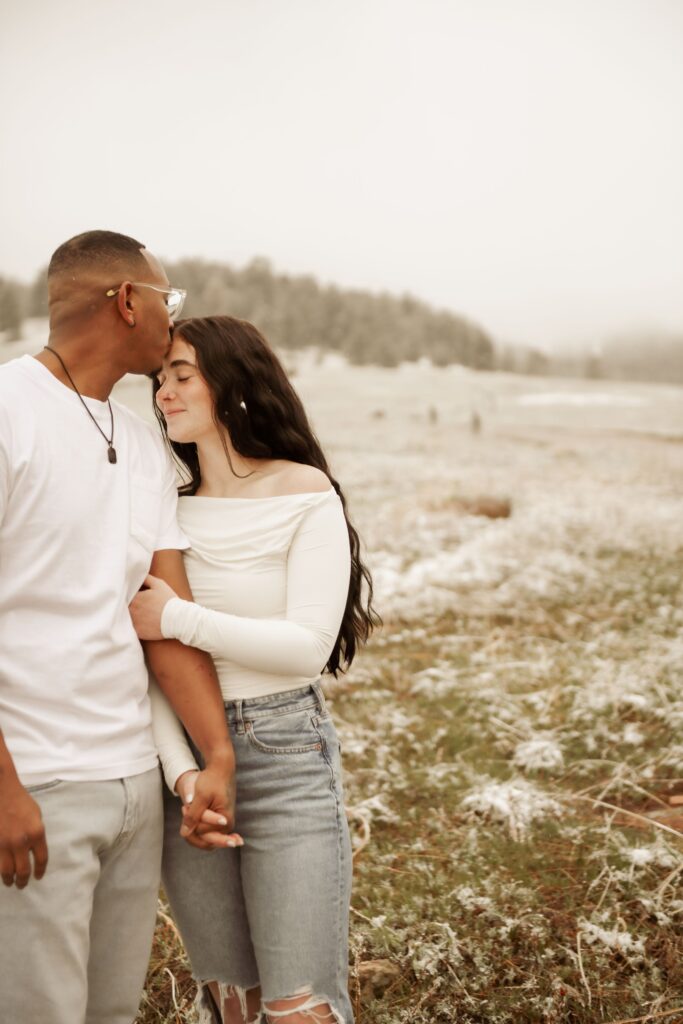 Man kissing his partner's forehead in a snowy field.

