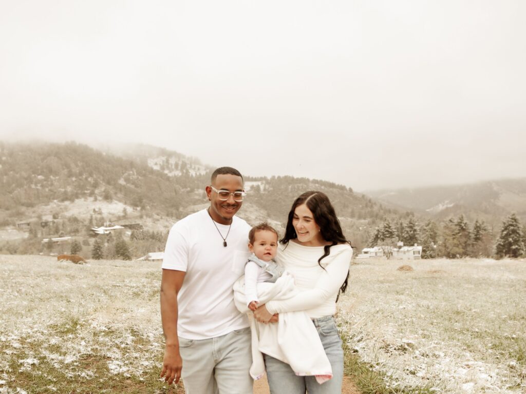 Family of three smiling together in a snowy mountain field.
