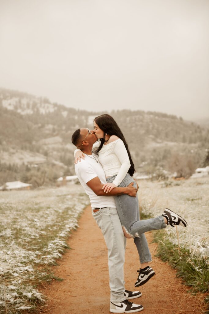 Man lifting his partner into a kiss on a path through a snowy landscape.