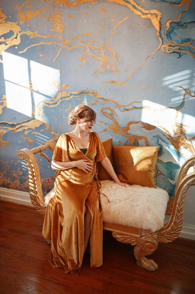 Pregnant woman posing on an elegant indoor chair during a maternity session.
