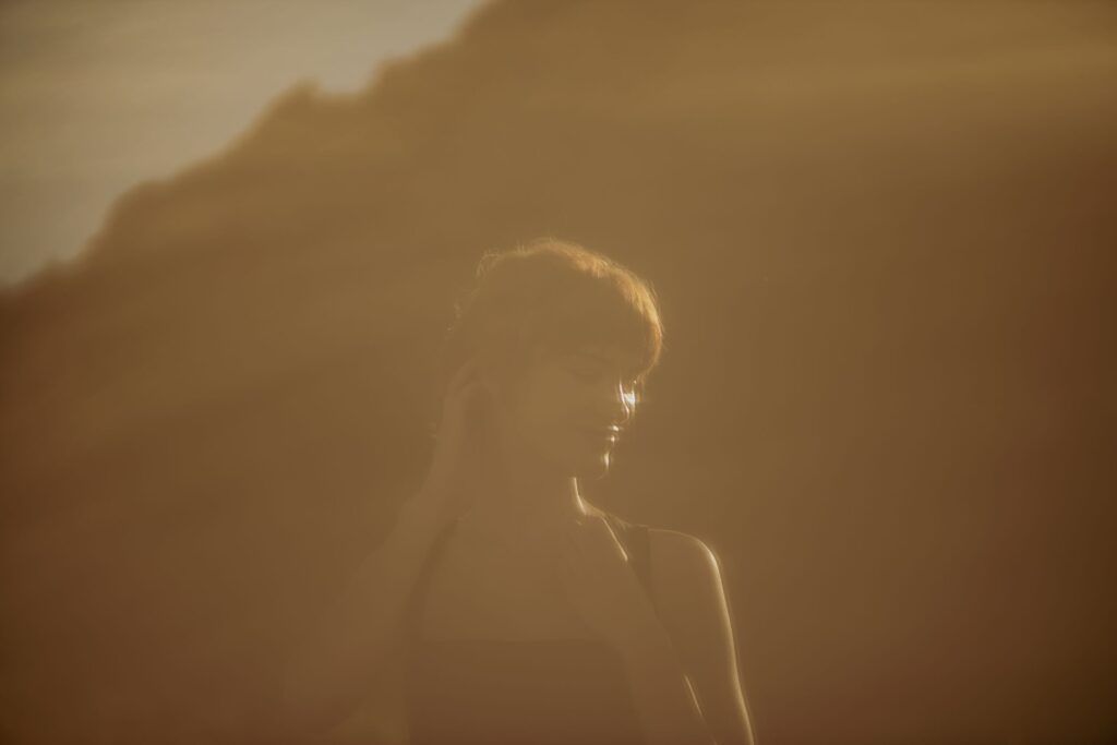 A backlit silhouette portrait of a woman in warm golden light with a mountain in the background.