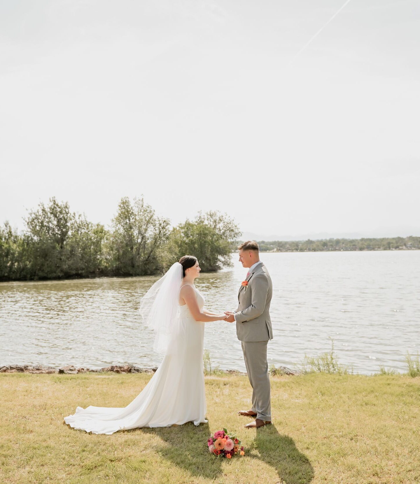 Bride and groom holding hands by a lakeside during their outdoor wedding ceremony.