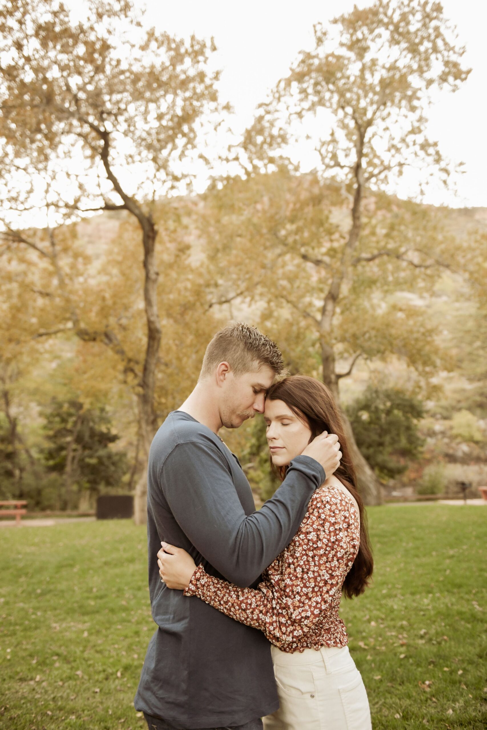 Couple embracing forehead to forehead under golden autumn trees.