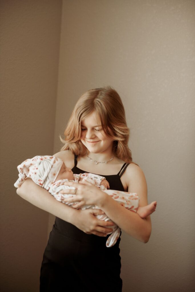 Older sister holding her newborn sibling with a smile.