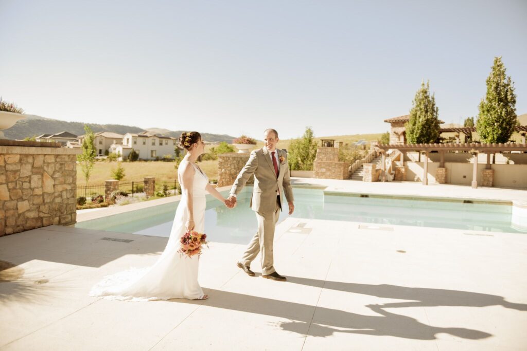 Bride and groom holding hands beside a pool on a stone patio
