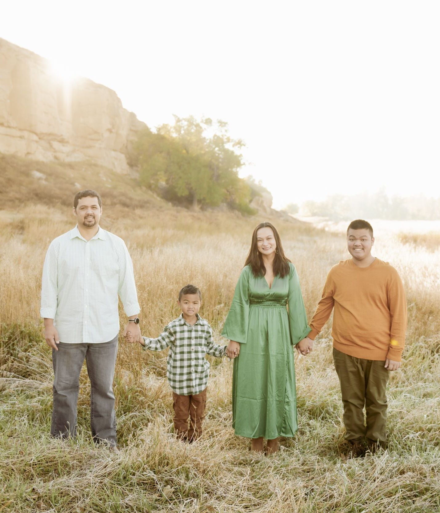 Family of four holding hands in a golden field near sunlit sandstone cliffs.