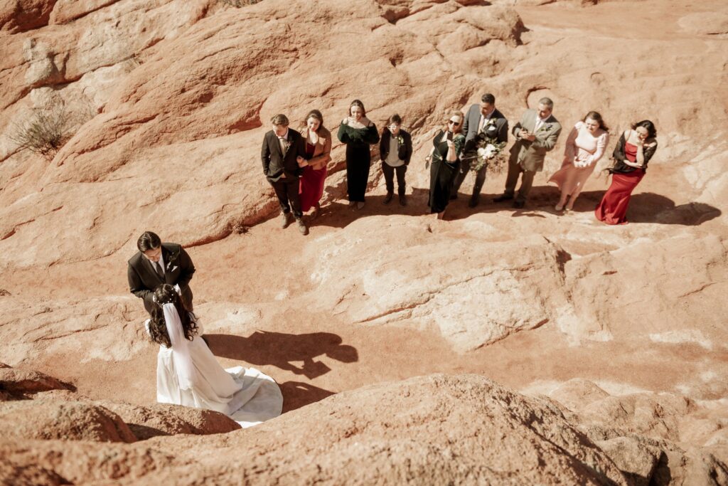 Wedding guests watching the couple exchange vows on red rock cliffs.