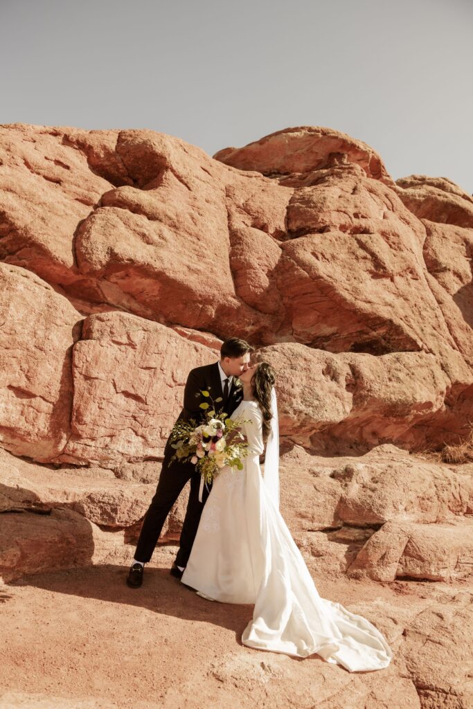 Bride and groom kissing in front of large red rock formations.