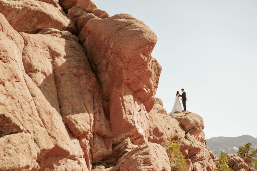 Bride and groom holding hands atop a large red rock formation.