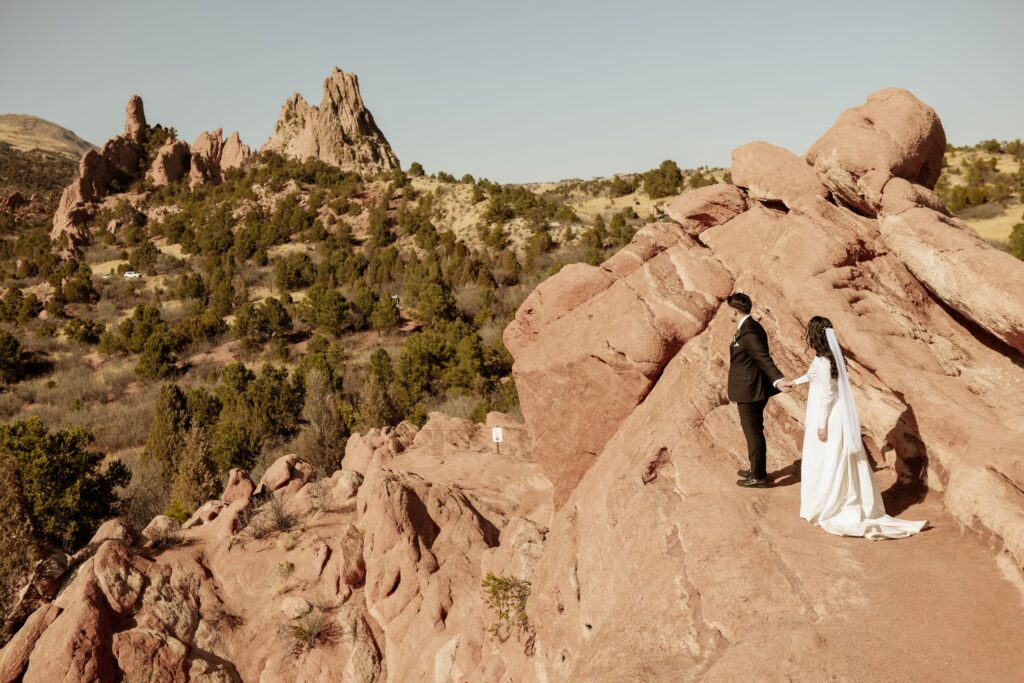 Bride and groom holding hands on red rock formations during their wedding.