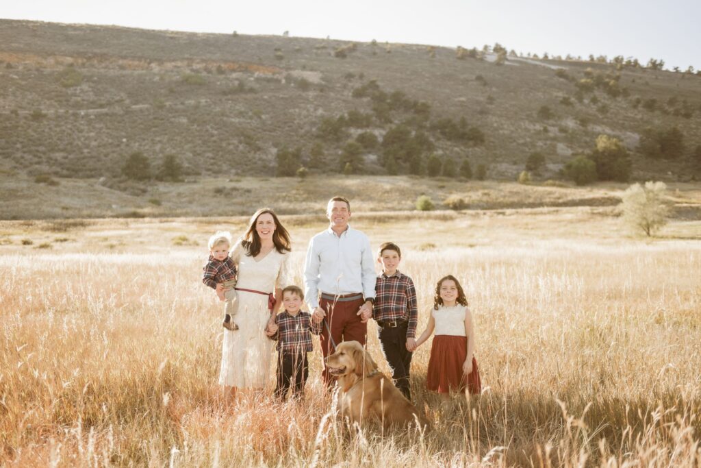 Family of six with their golden retriever standing in a sunlit field.