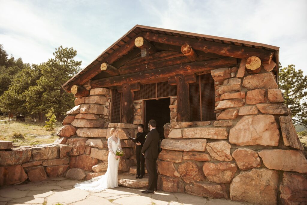 Bride and groom exchanging vows with an officiant outside a rustic stone chapel.
