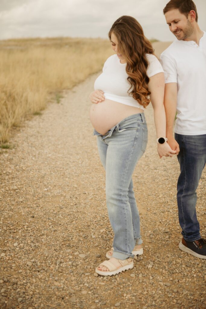 Pregnant couple holding hands on a gravel path during maternity session