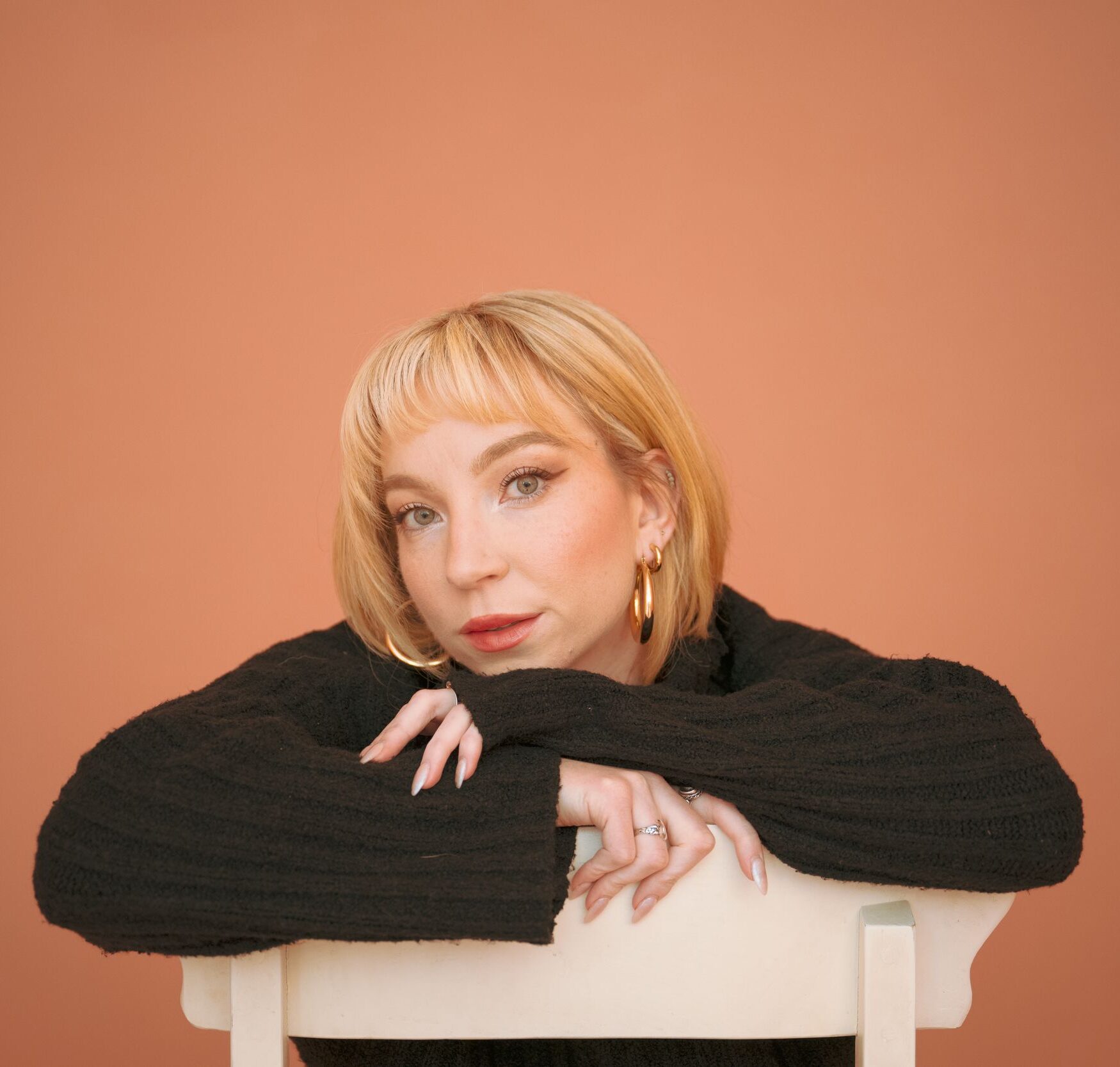 Woman with short blonde hair posing against a peach background